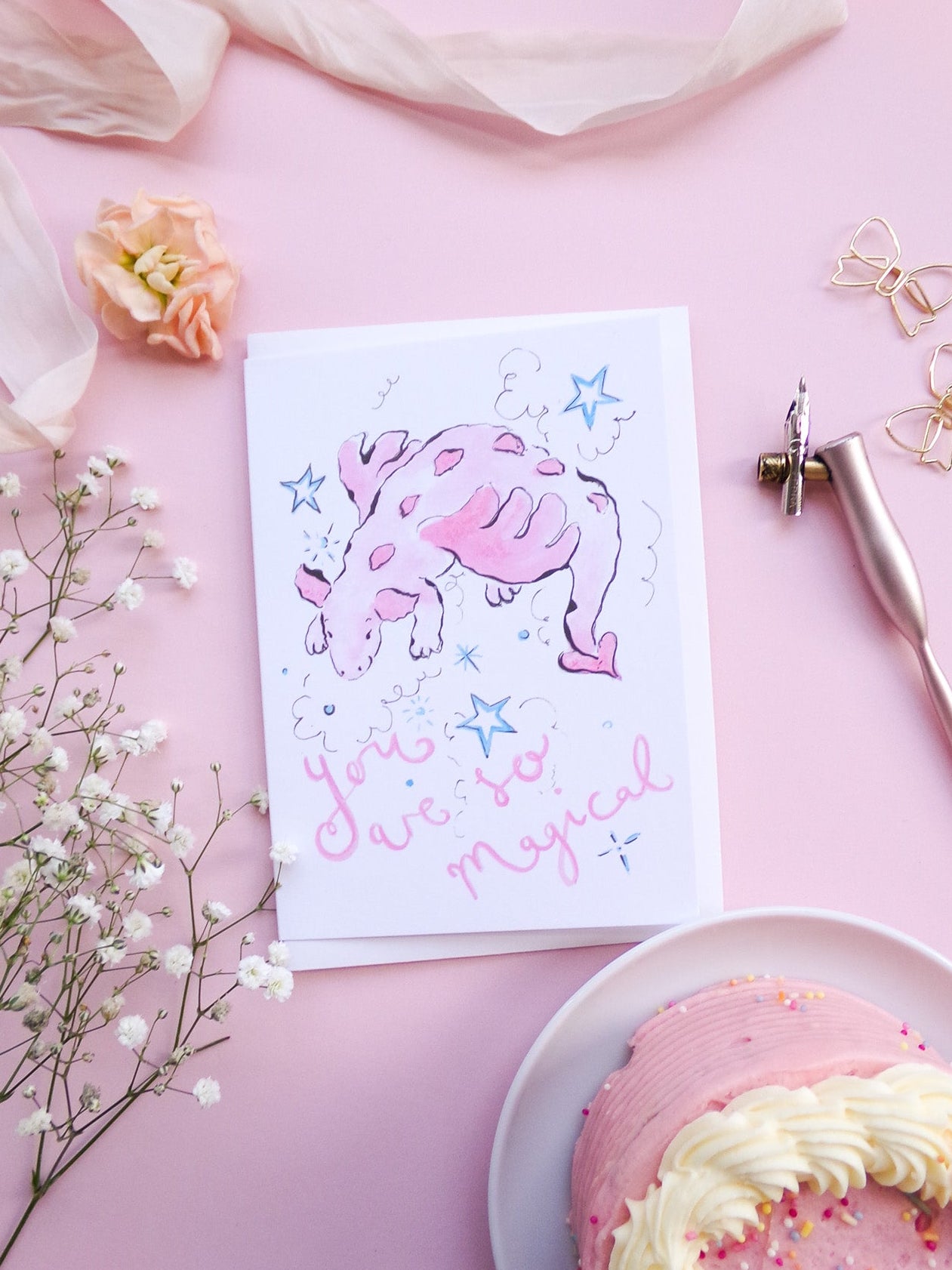 Card with a pink elephant and text 'You are so magical' on a pink background with flowers and a cake.