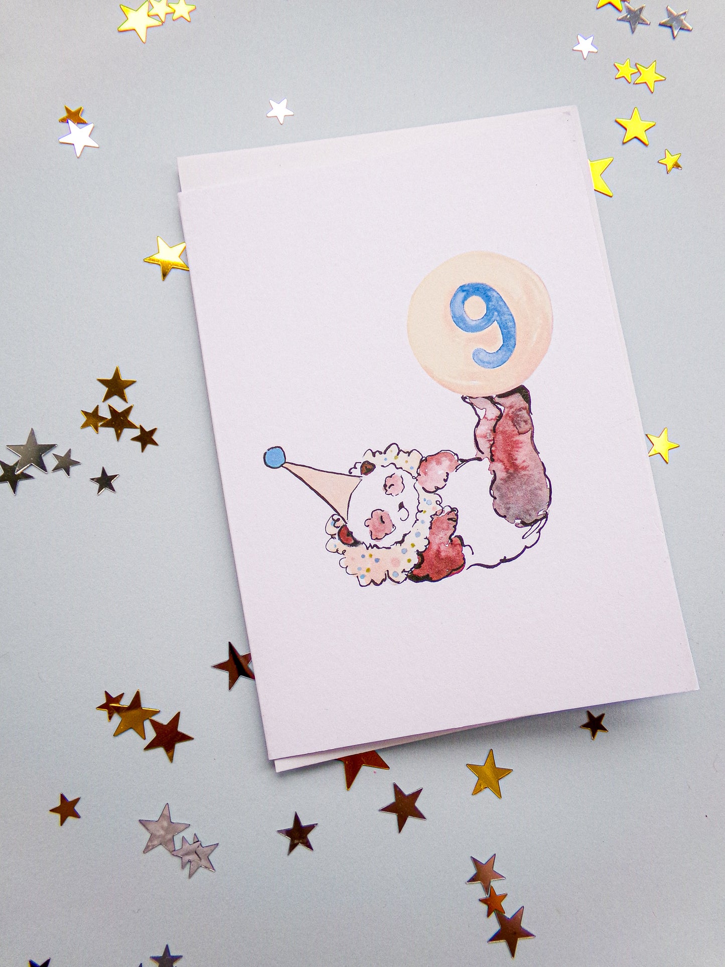 Card with a clown design and number 9 on a gray background with star confetti
