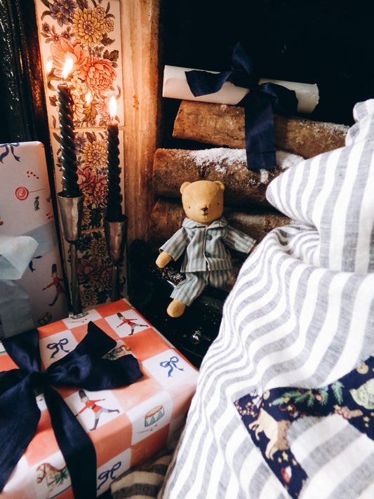 Teddy bear sitting on a bed next to wrapped gifts with decorative ribbons.