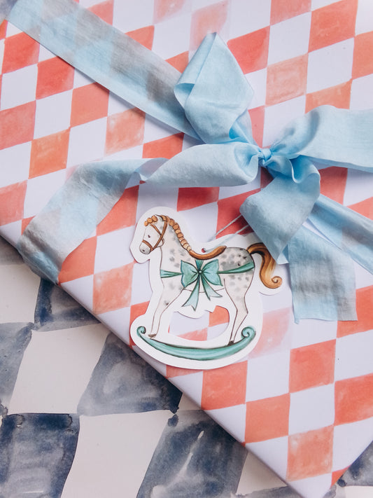 Gift wrapped in checkered paper with a blue ribbon and a decorative label of a rocking horse.