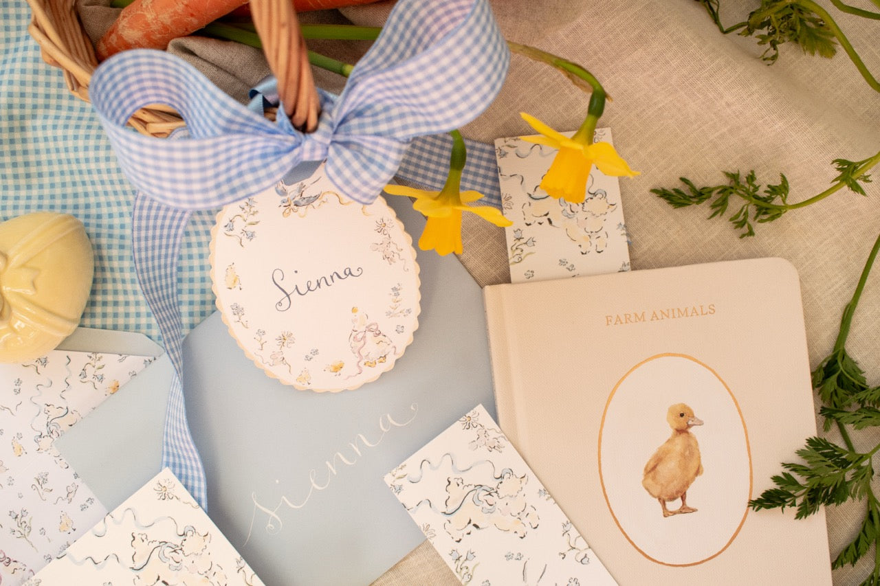 Assorted items including a basket, decorative plates, and cards on a soft surface with flowers.