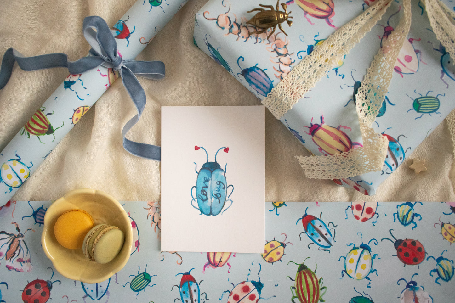 Gift wrap with colorful beetle design, a card, and a small bowl on a matching background.