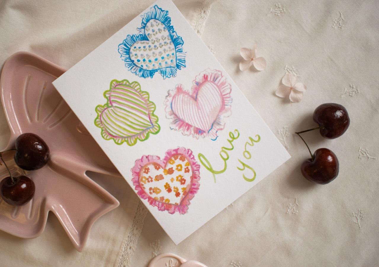 Card with heart designs and 'love you' text on a textured surface with cherries.