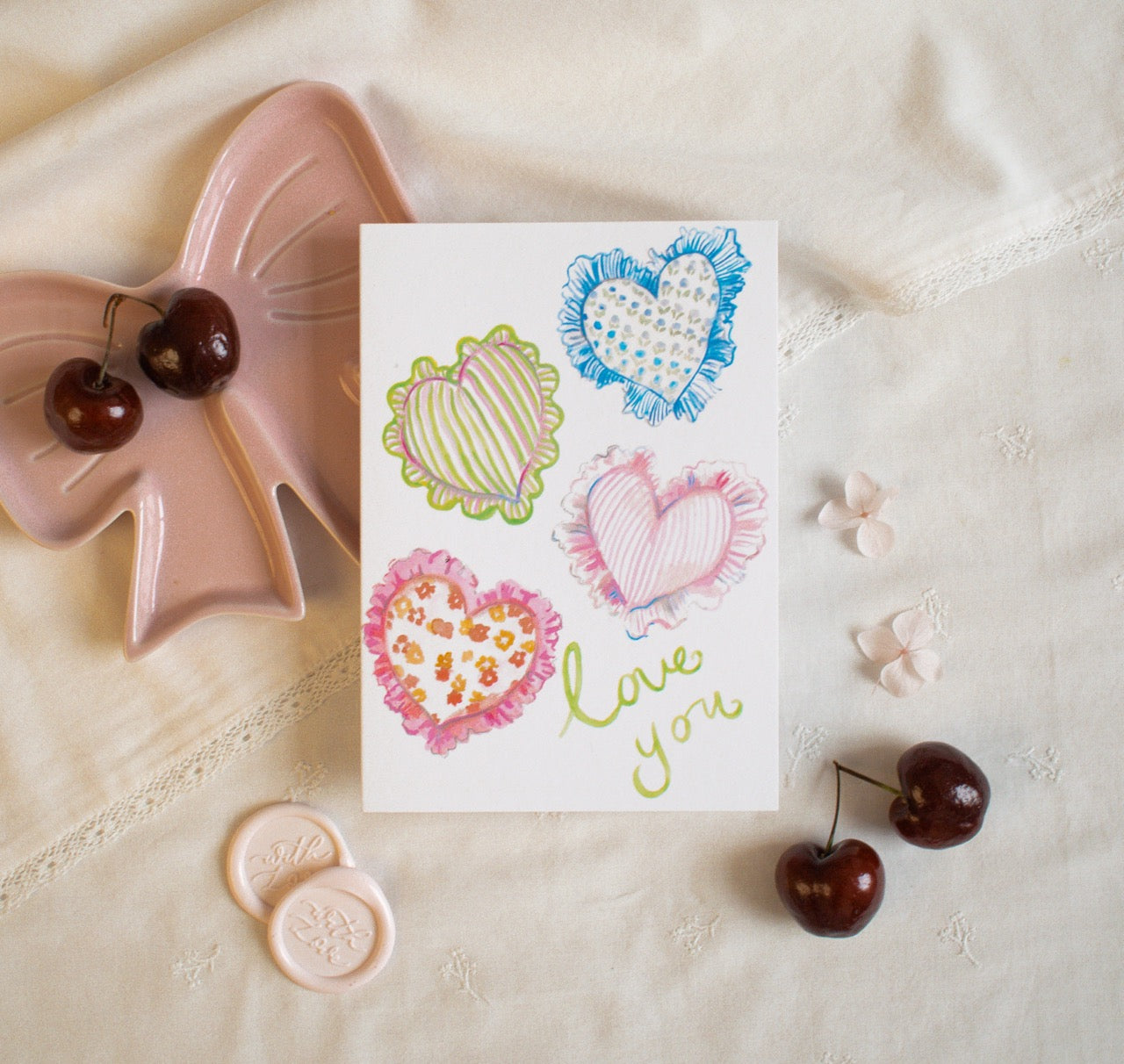 Card with heart designs and 'love you' text on a textured surface with decorative items.