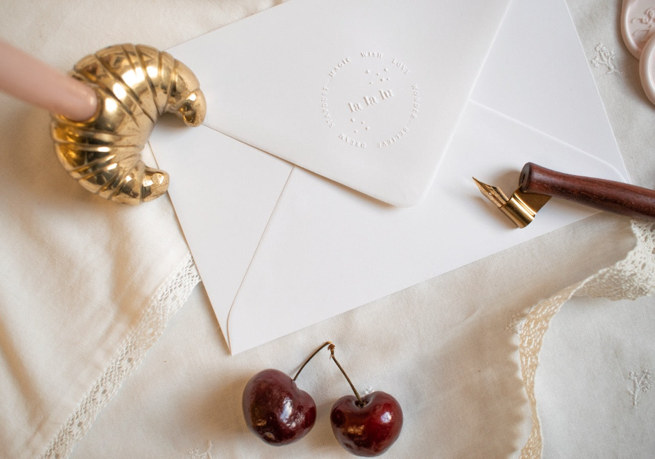 Envelopes, cherries, and a gold pen on a textured surface