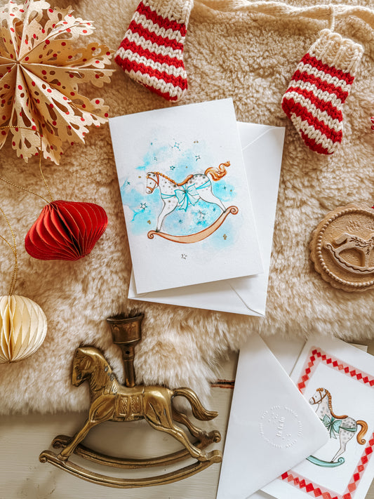 Christmas card with a rocking horse design on a decorative surface with ornaments.