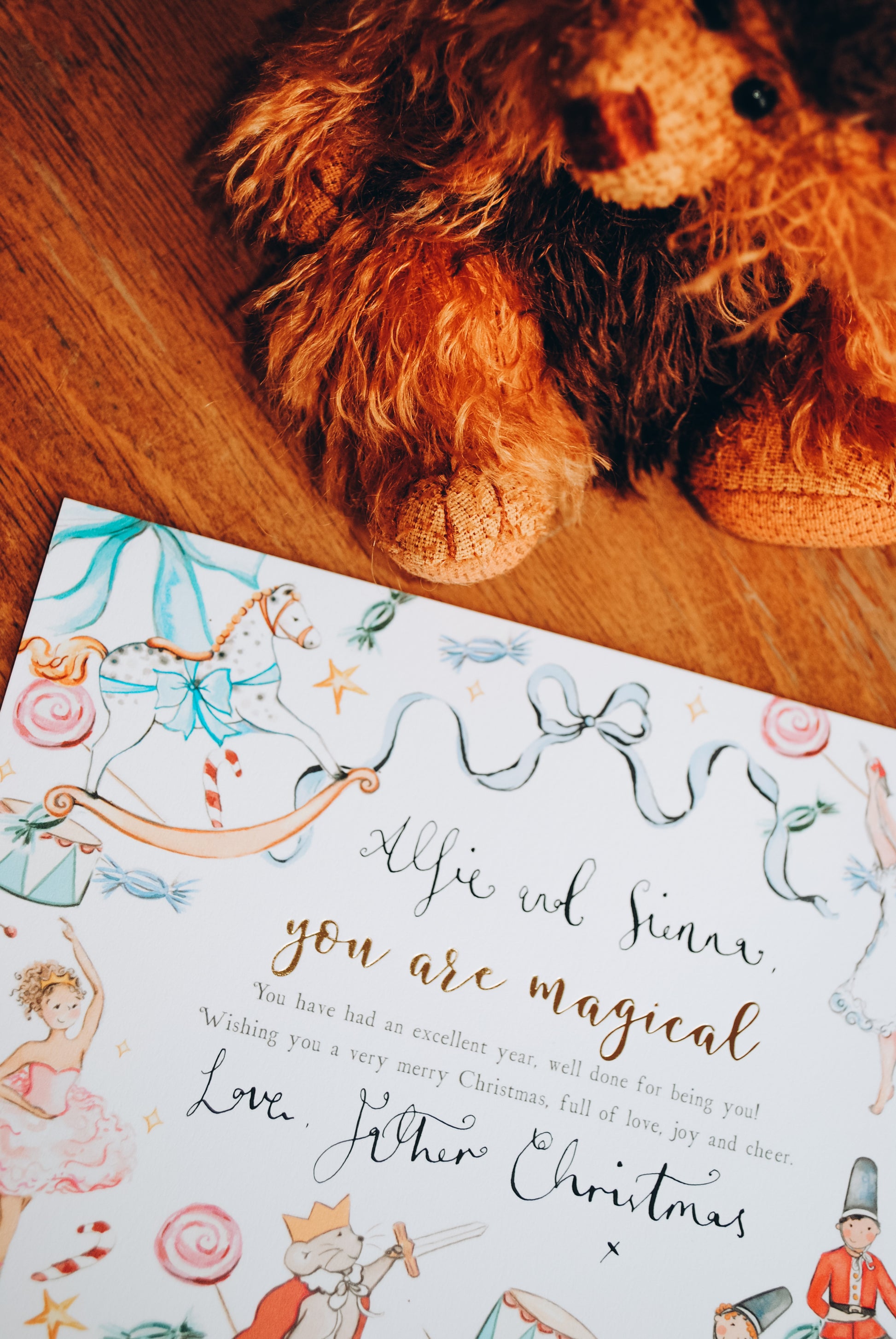 Stuffed lion toy next to a Christmas card with decorative elements on a wooden surface