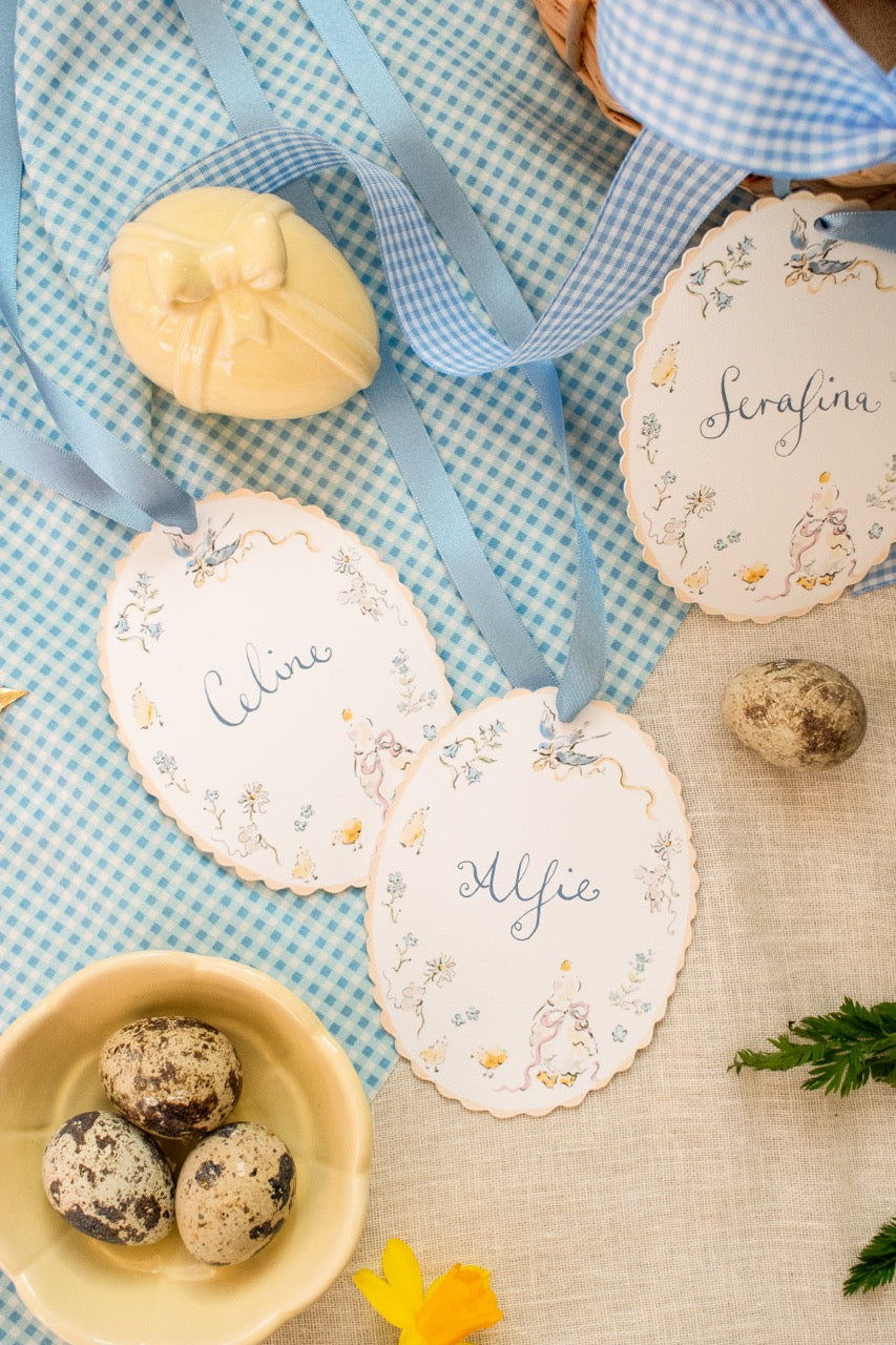 Decorative Easter egg cards with names on a checkered tablecloth with eggs and ribbons.