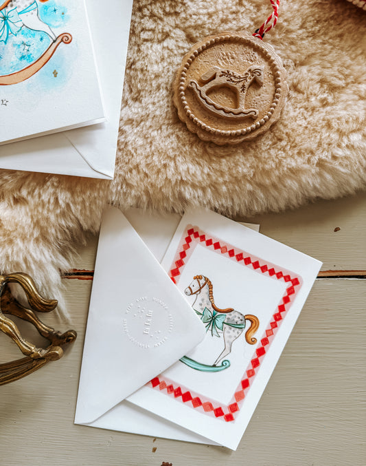 Decorative greeting card with a reindeer design, envelope, and cookie on a textured surface.