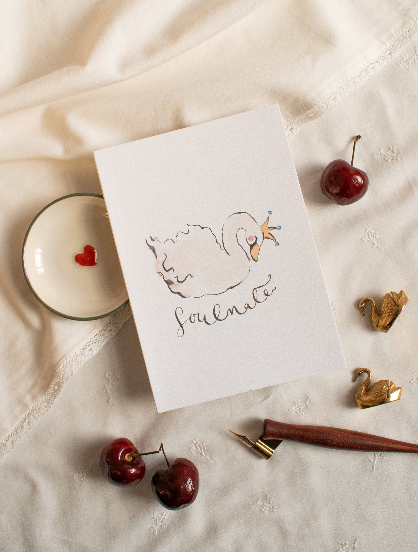 Card with a swan illustration and 'Soulmate' text on a textured surface with cherries and a pen.