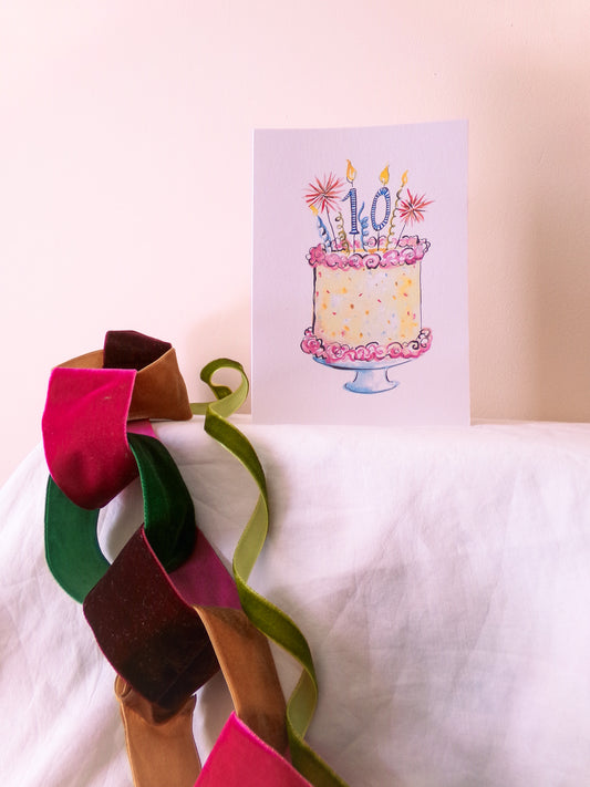 Colorful ribbons on a white surface with a birthday cake card in the background