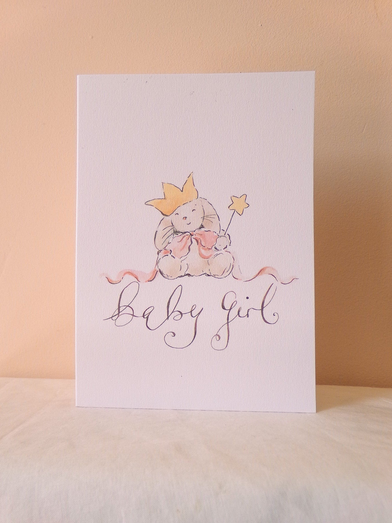 Greeting card with a baby girl illustration and 'baby girl' text on a beige background