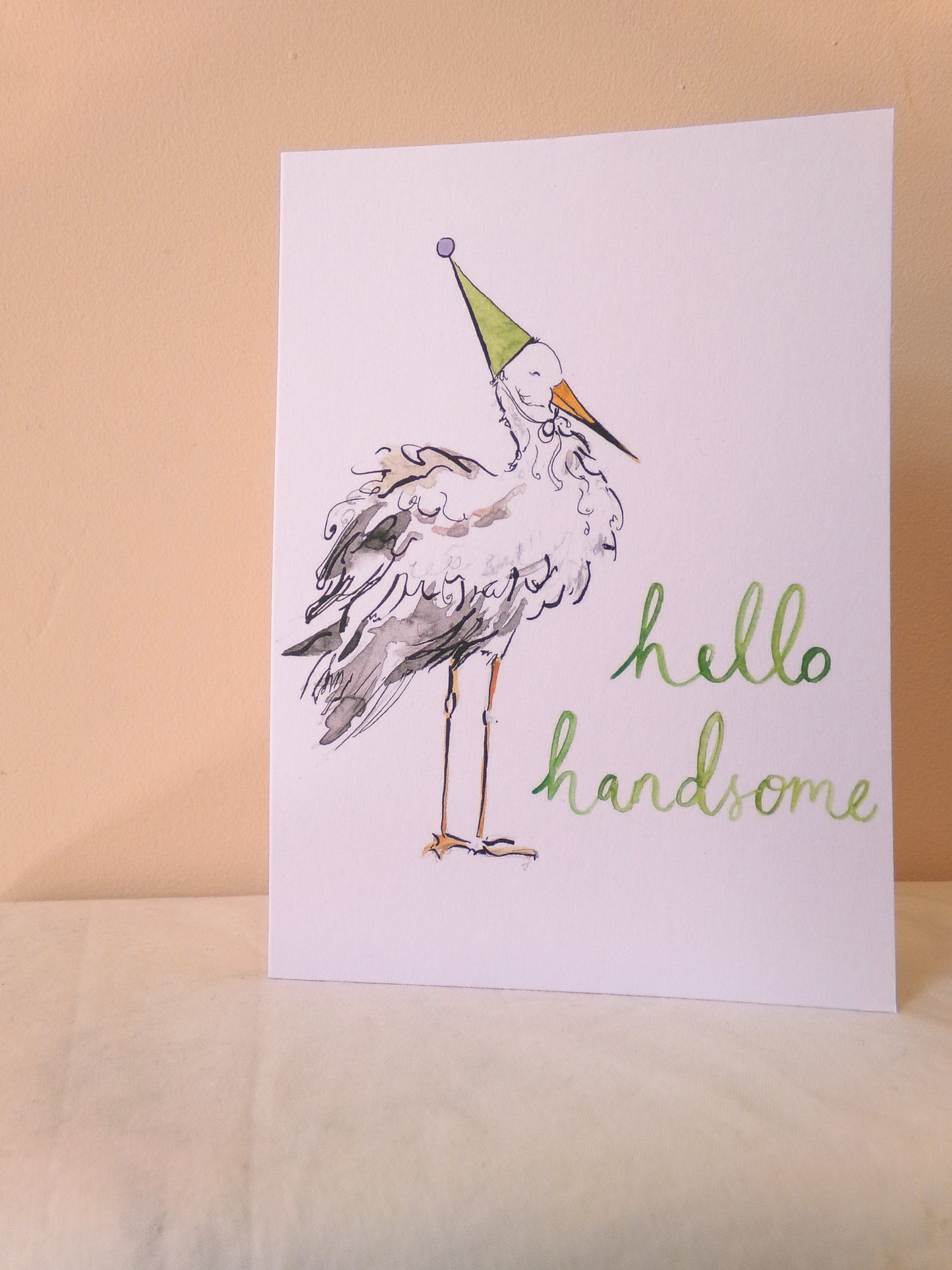 Card with a stork wearing a party hat and 'hello handsome' text on a beige background