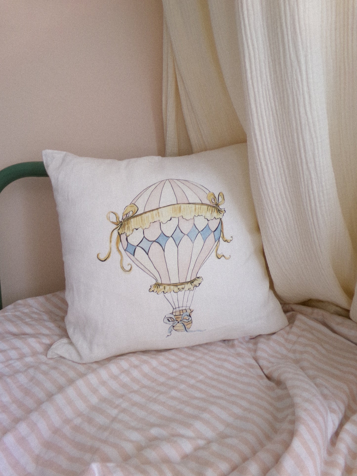 Decorative pillow with hot air balloon design on a bed with pink bedding.