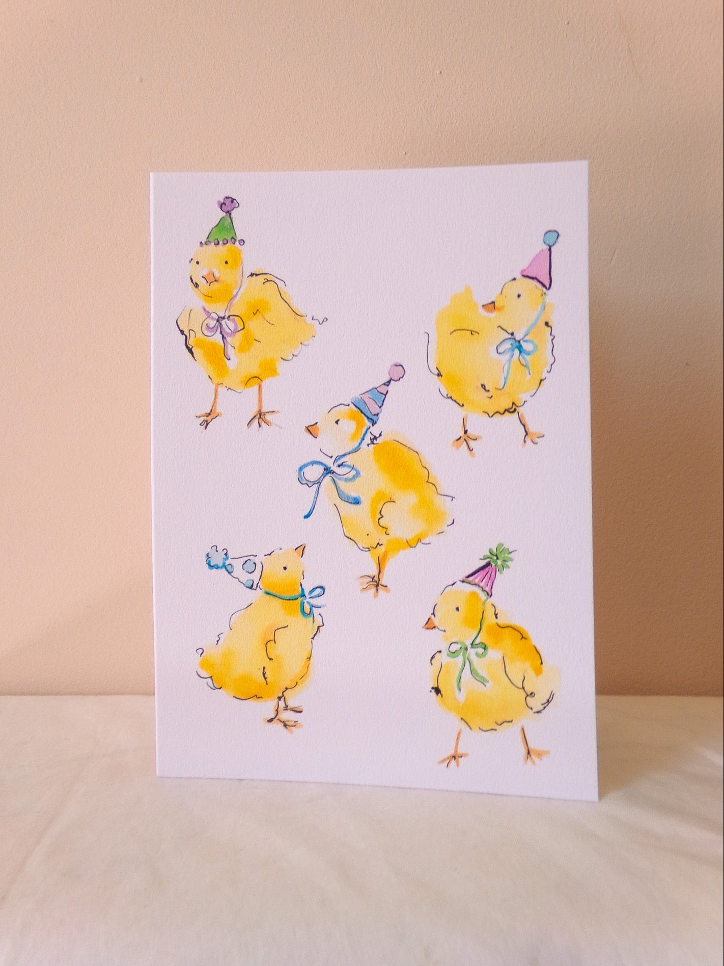 Card with illustrations of yellow chicks wearing party hats on a beige background