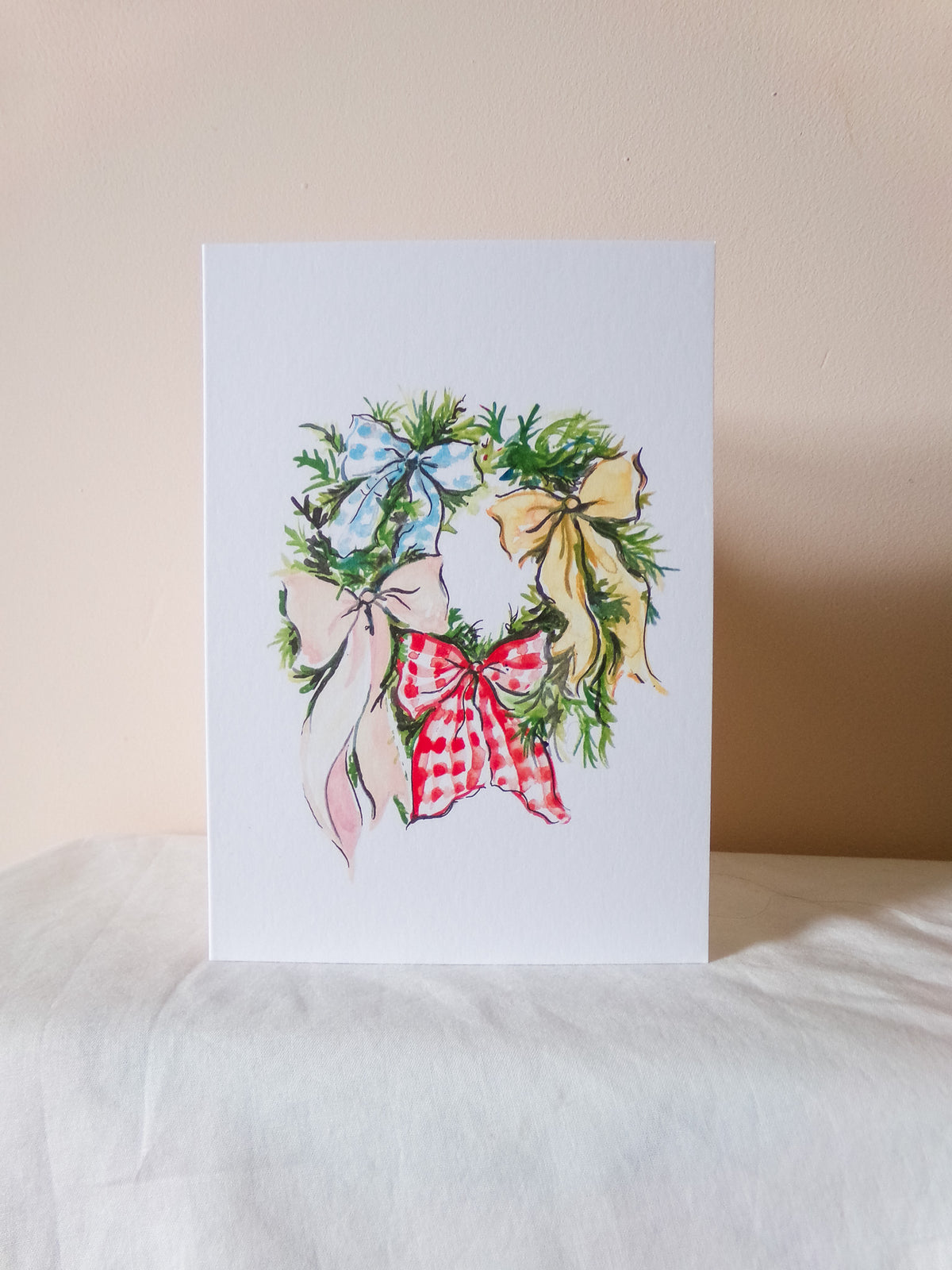 Greeting card with a festive wreath design featuring colorful bows on a beige background.