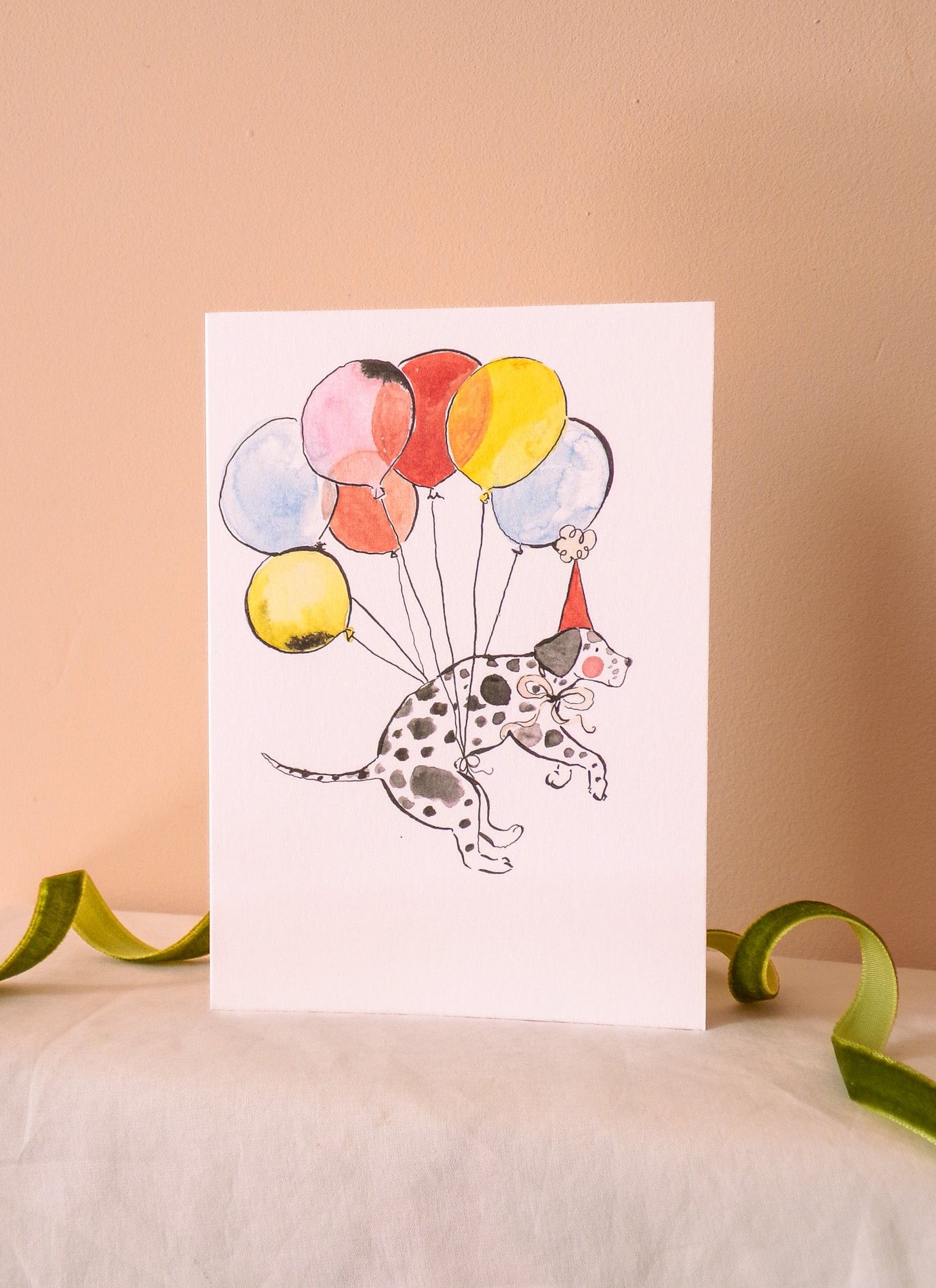 Greeting card with a dalmatian dog holding colorful balloons on a beige background