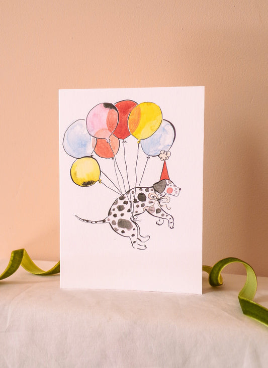 Greeting card with a dalmatian dog holding colorful balloons on a beige background