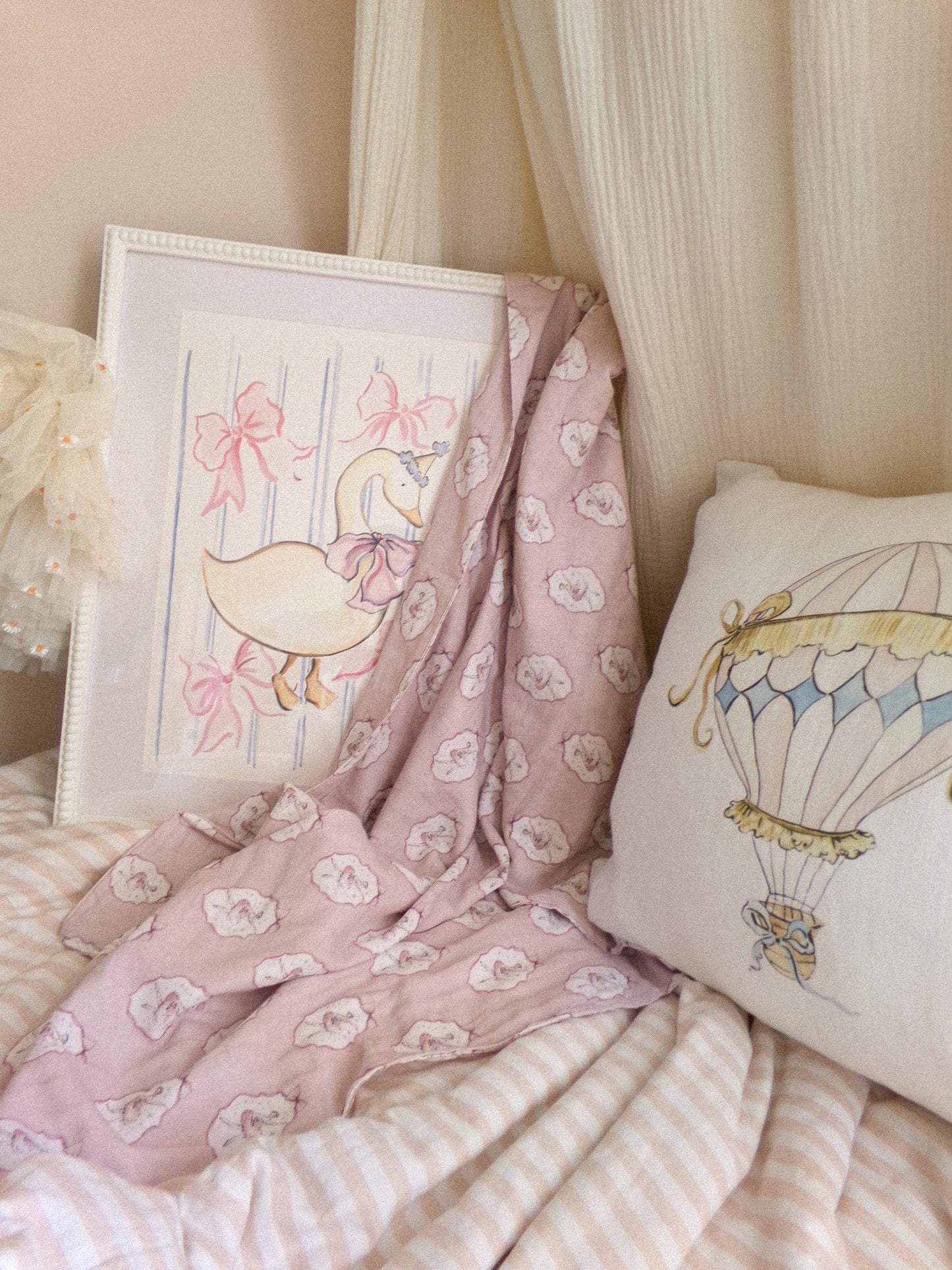 Pink floral blanket, framed artwork, and decorative pillow on a bed with light curtains.