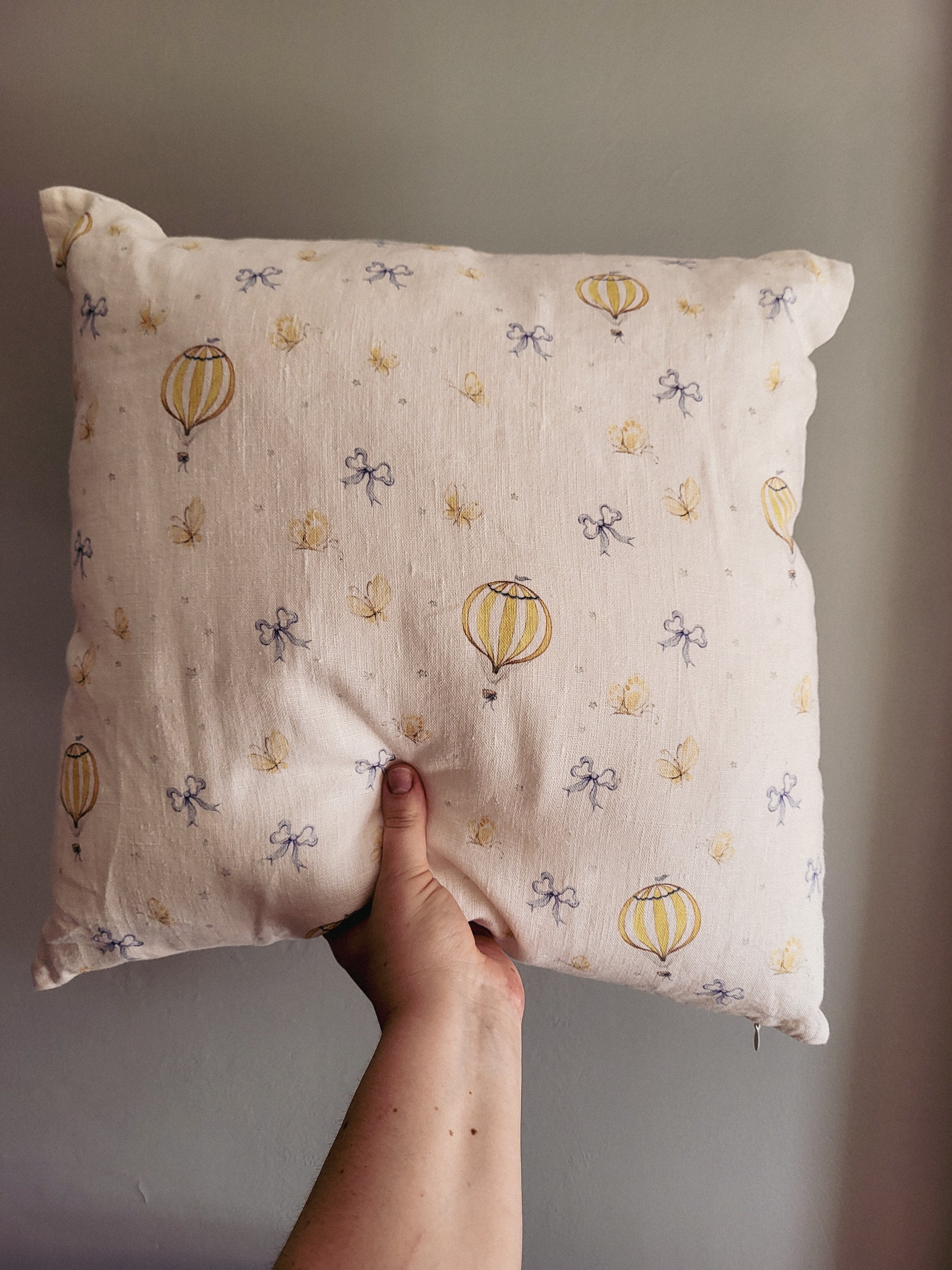 Hand holding a pillow with hot air balloon pattern against a plain background