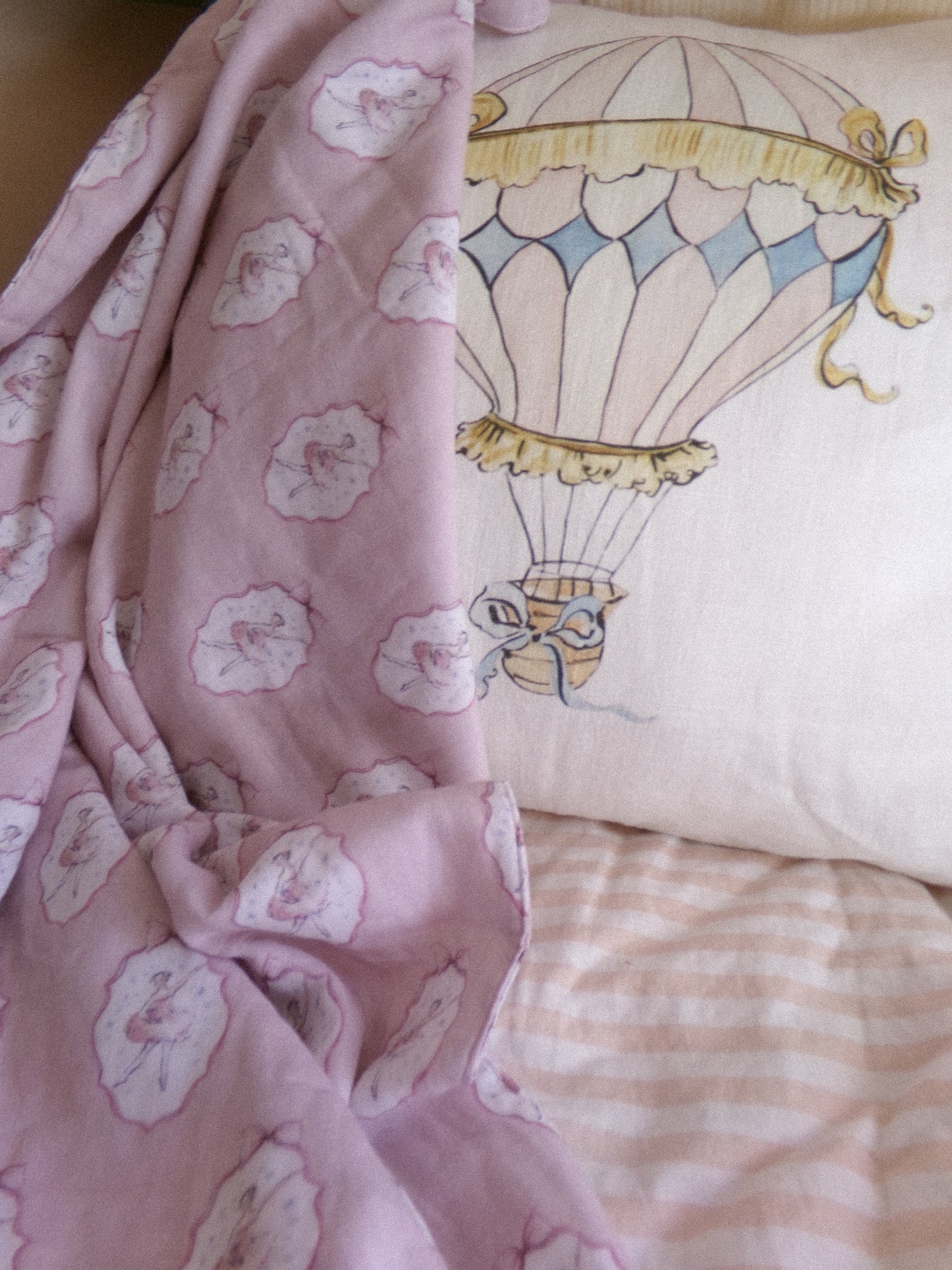 Pink floral blanket and pillow with hot air balloon design on a bed.