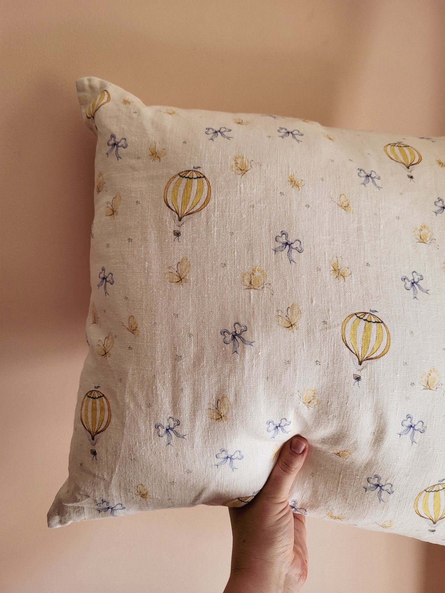 Hand holding a pillow with hot air balloon and bow pattern against a beige background