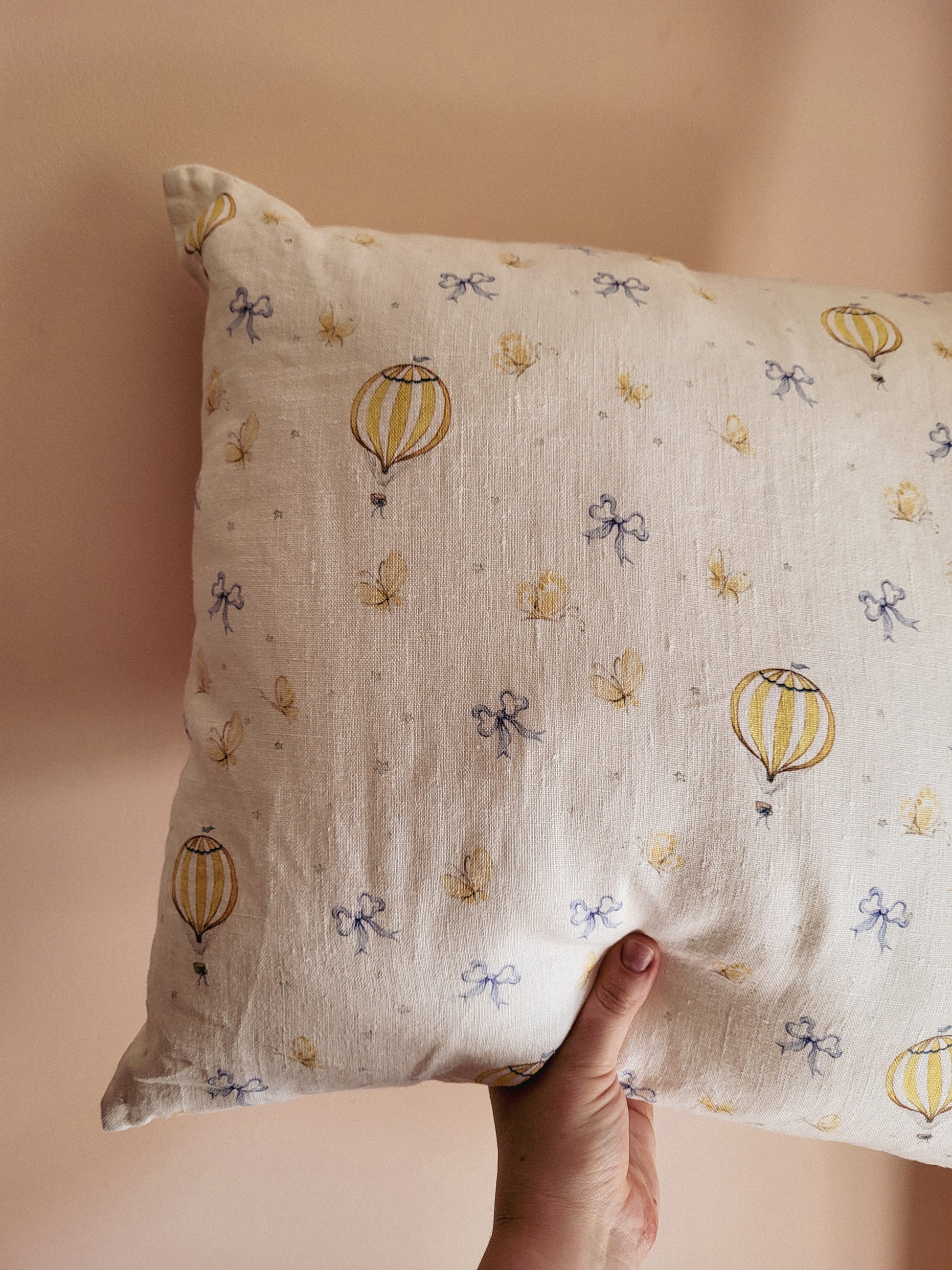 Hand holding a pillow with hot air balloon and bow pattern against a beige background