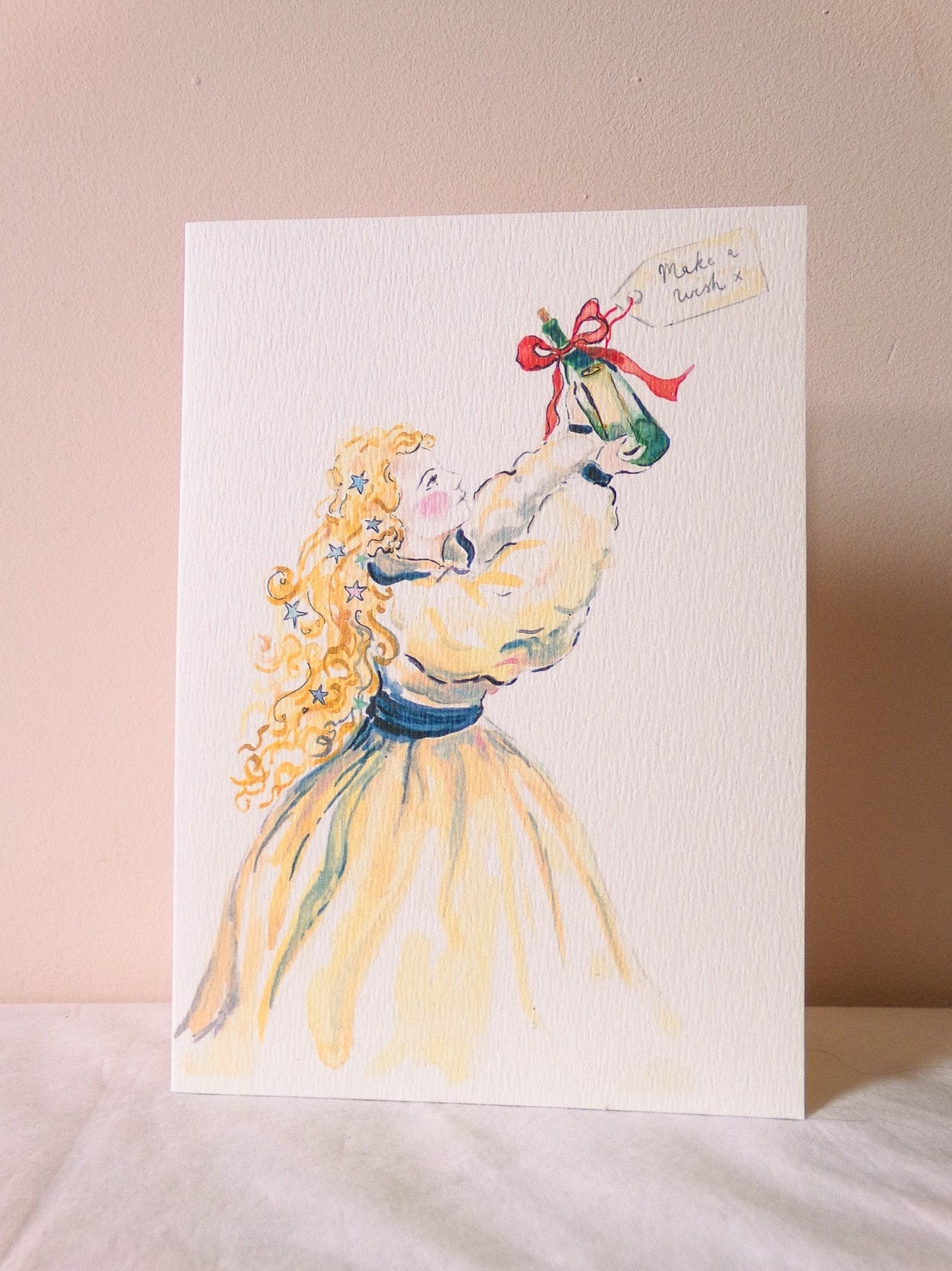 Greeting card with a watercolor illustration of a woman in a yellow dress holding a green hat on a pink background.