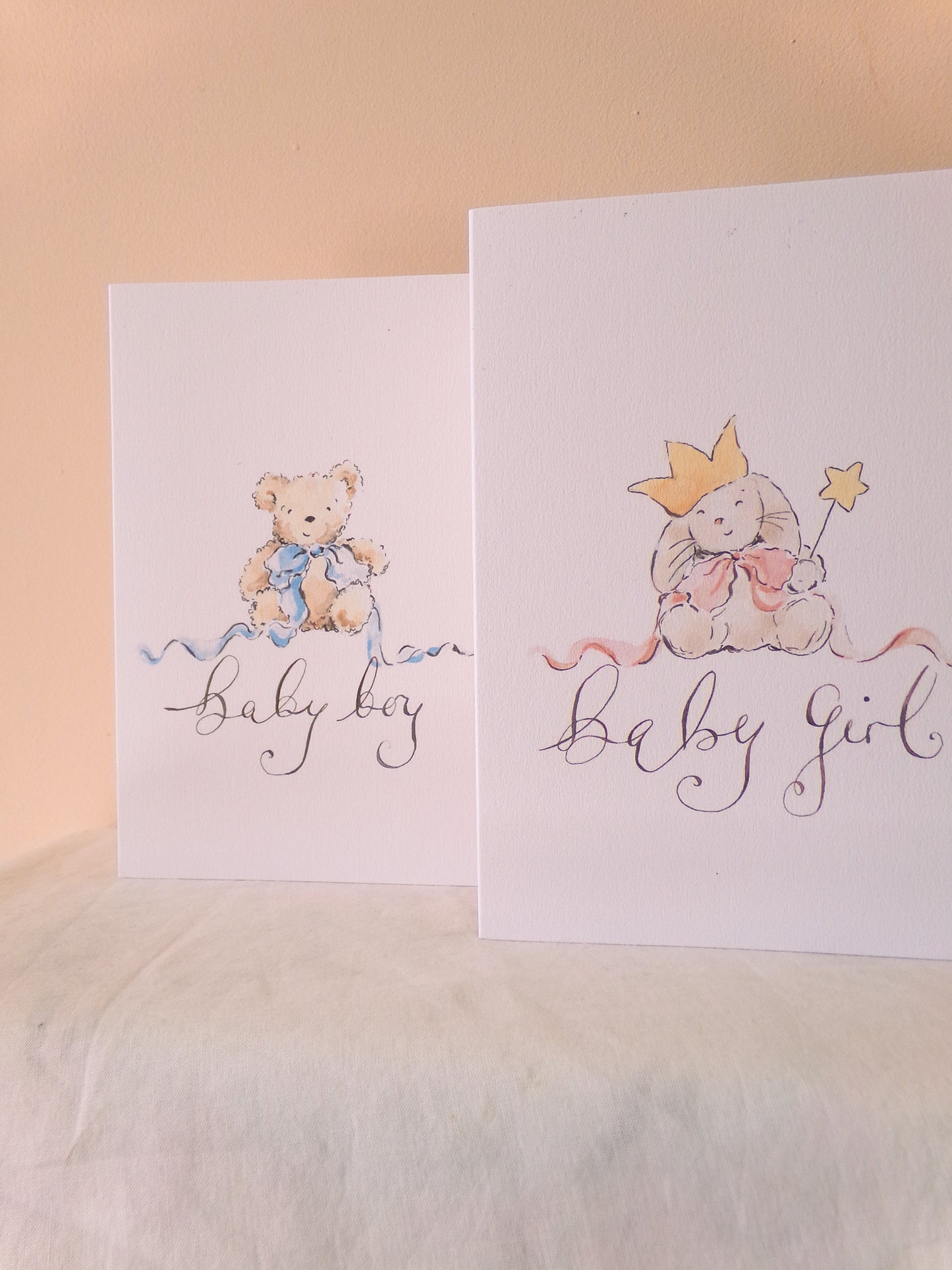Two greeting cards for baby boy and girl on a soft surface with a pink background.