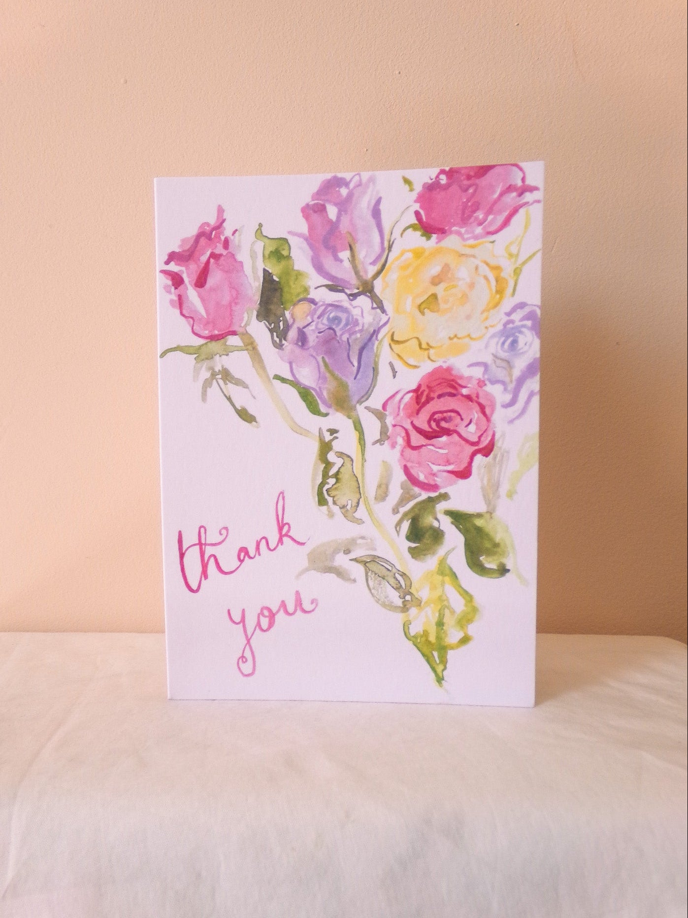 Greeting card with watercolor flowers and 'thank you' text on a soft surface.