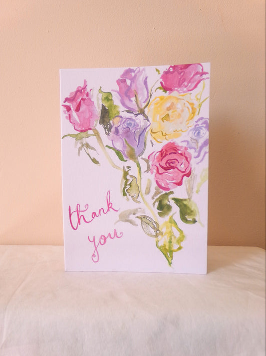 Greeting card with watercolor flowers and 'thank you' text on a soft surface.